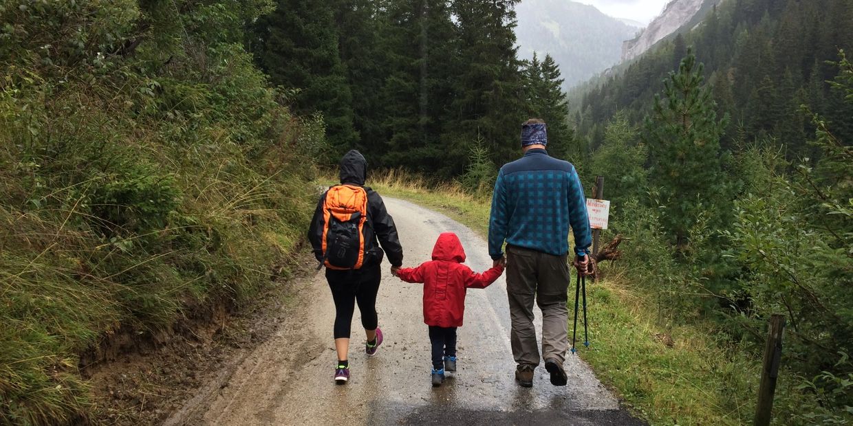 Mother, son, and father taking a walk in the rain on a road through the forest.