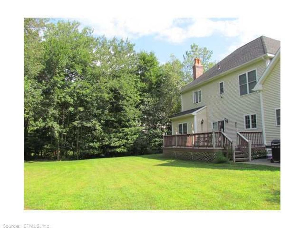Backyard with green lawn and a two-story house featuring a wooden deck.