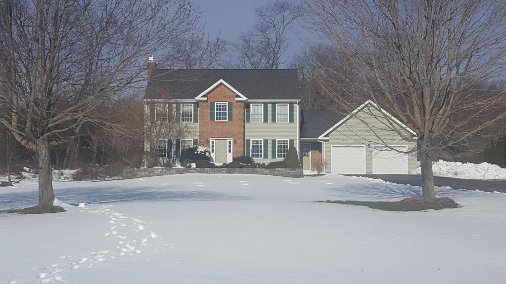 Two-story house with snow-covered yard and bare trees on a clear winter day.