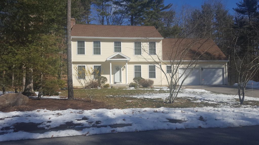 Two-story beige house with snow on the ground and bare trees.