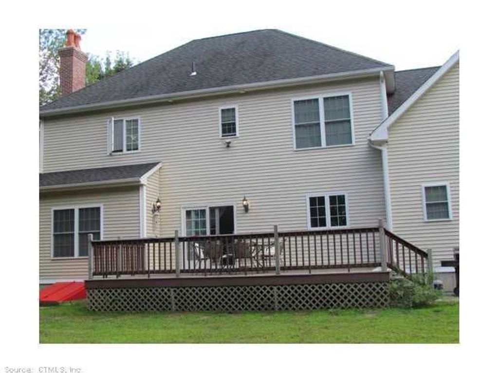 Backyard deck with wooden railing attached to a two-story house with beige siding.