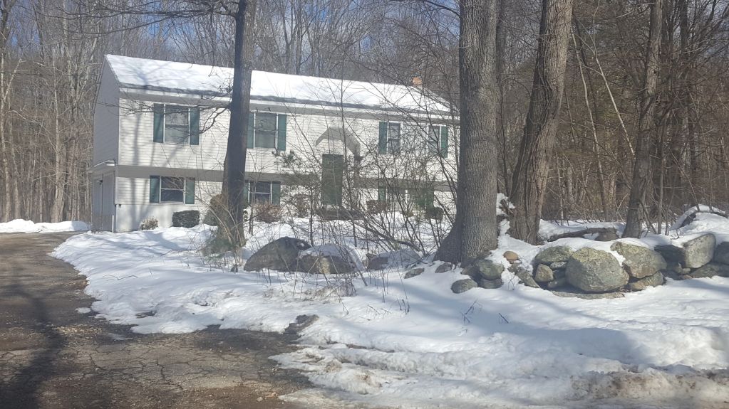 A white house surrounded by snow and trees on a sunny winter day.