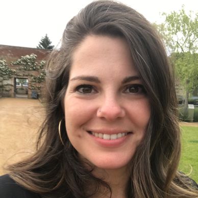 Smiling woman outdoors with trees in the background.