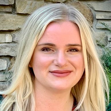 Smiling woman with long blonde hair in front of a stone wall.