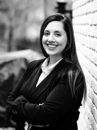 Confident woman smiling while leaning against a brick wall outdoors.