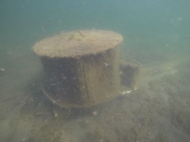 Underwater view of a rusted cylindrical object on the seabed.