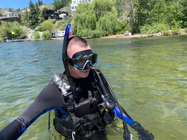 A diver in full gear emerging from clear water on a sunny day.