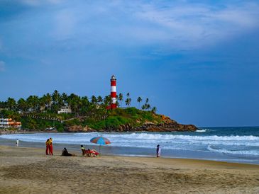 Lighthouse on a green hill by the beach with people on the shore.
