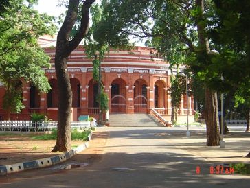 A historic red brick building with arches surrounded by trees.