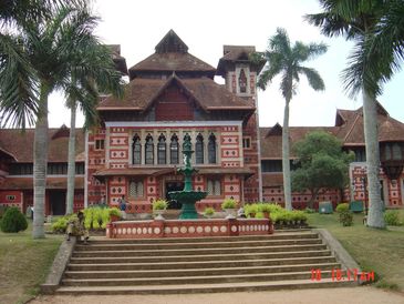 Historic red and white building with palm trees and a central fountain.