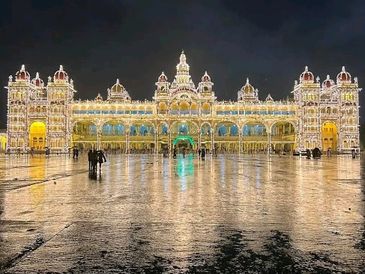 Illuminated palace at night with reflections on wet ground.