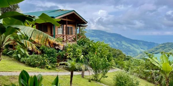Wooden cabin surrounded by lush greenery and mountains.
