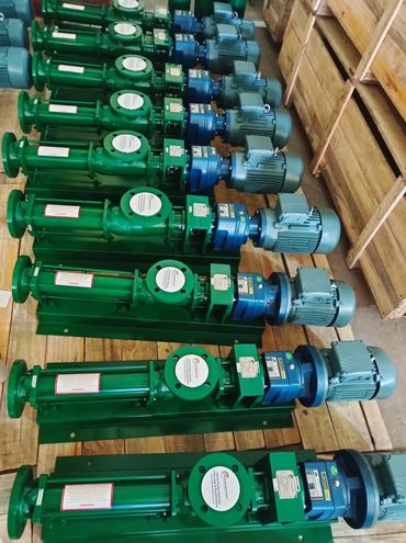 Row of green industrial pumps with blue motors arranged on a wooden floor.