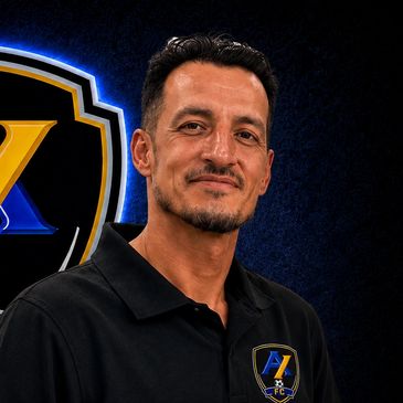 Man in black polo shirt with logo against dark background.