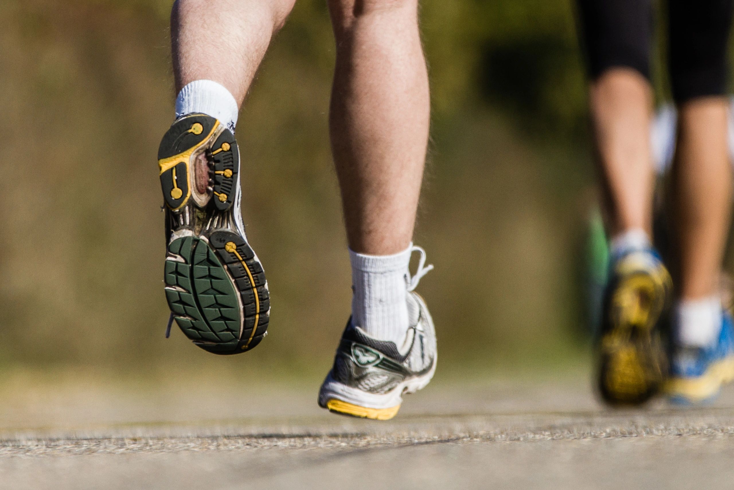 Close-up of runners' shoes and legs in mid-stride on a path.