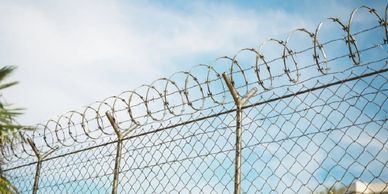 Chain-link fence topped with barbed wire under a clear blue sky.