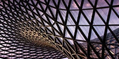 Intricate geometric glass ceiling with curved design and evening sky.