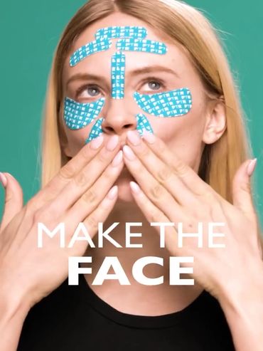 Woman with blue facial patches touching her lips against green background.