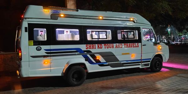 White travel van with 'SHRI KD TOUR AND TRAVELS' parked at night.