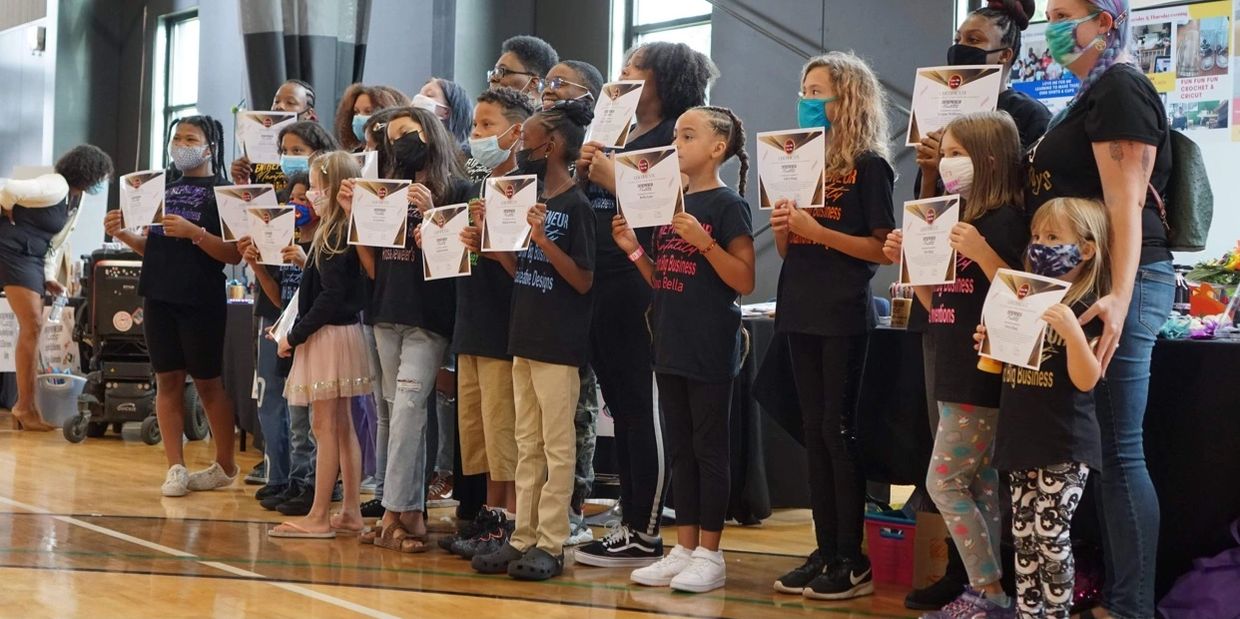 Children and adults proudly display certificates in a gymnasium setting.