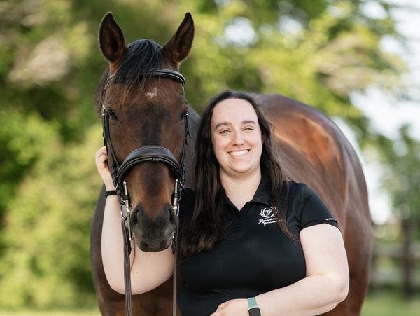 Smiling woman posing with a brown horse outdoors.