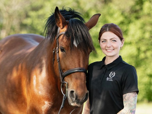 Woman standing next to a brown horse outdoors.