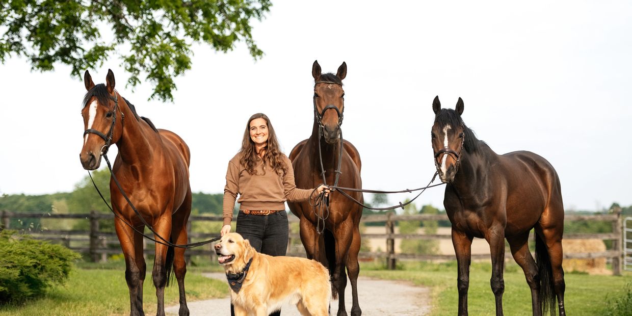 Girl standing with three horses and a golden retriever.