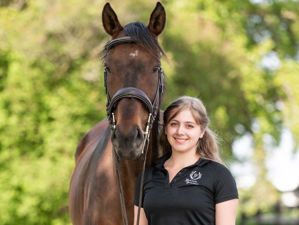Young woman standing next to a brown horse.