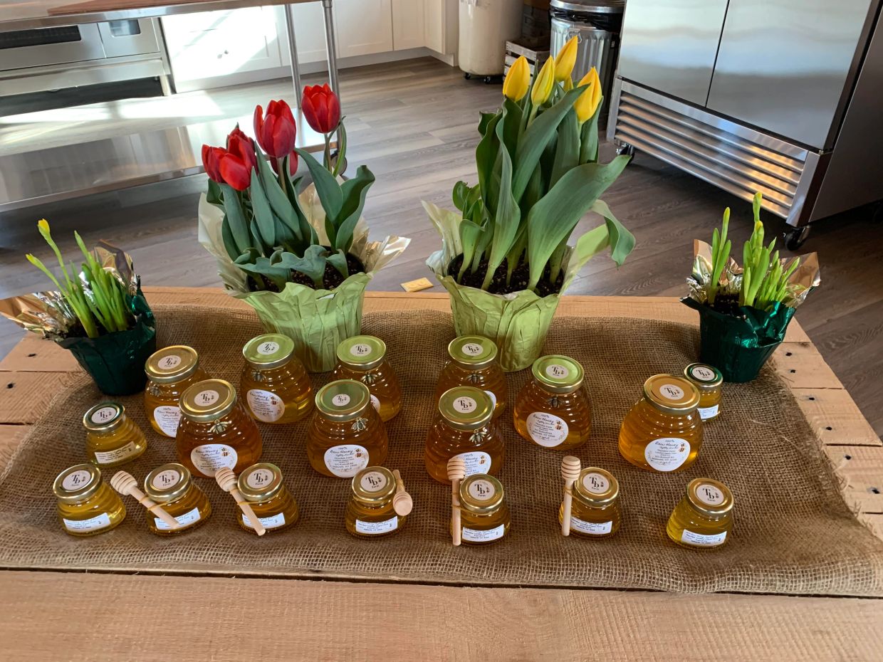 Jars of honey arranged on a table with red and yellow tulip plants.