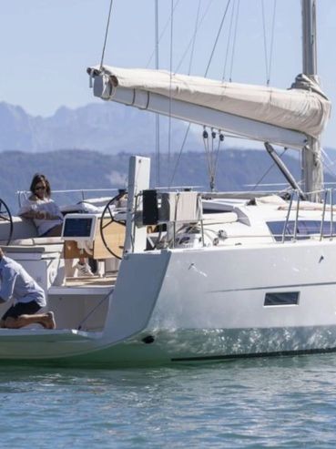 People relaxing on a white sailboat in calm waters with mountains in the background.