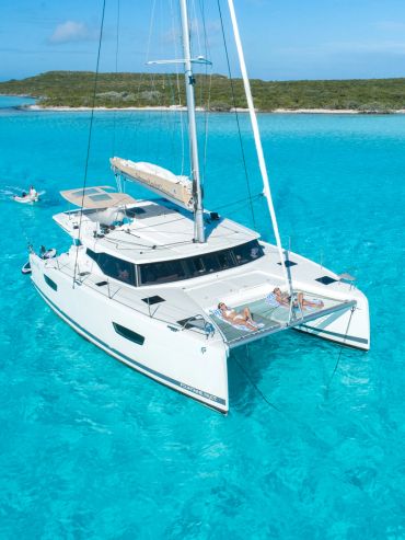 A white catamaran yacht sailing on clear turquoise water near an island.