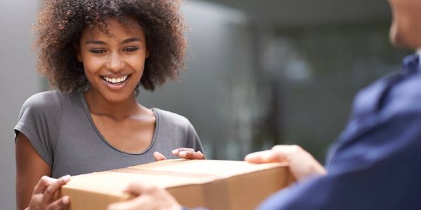 A smiling woman receiving a package from a delivery person.