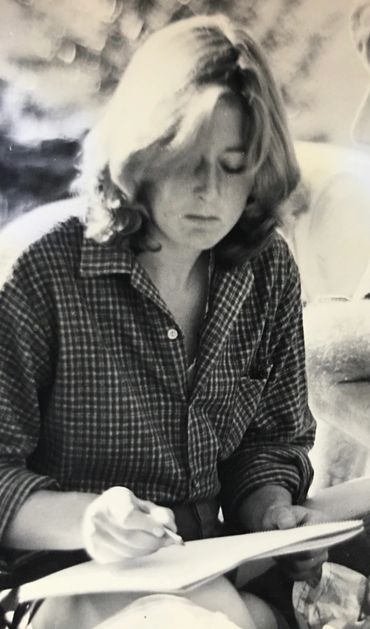 Woman writing or drawing on paper outdoors.