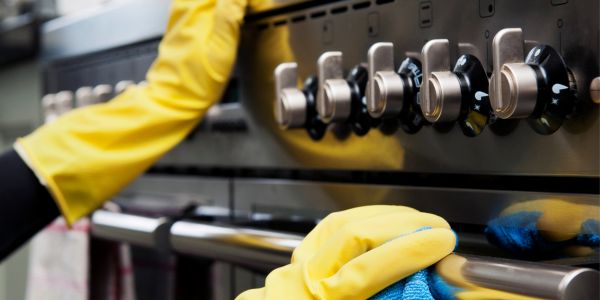 Person cleaning a stainless steel oven while wearing yellow gloves.