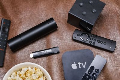 Various remote controls and a bowl of popcorn on a leather surface.