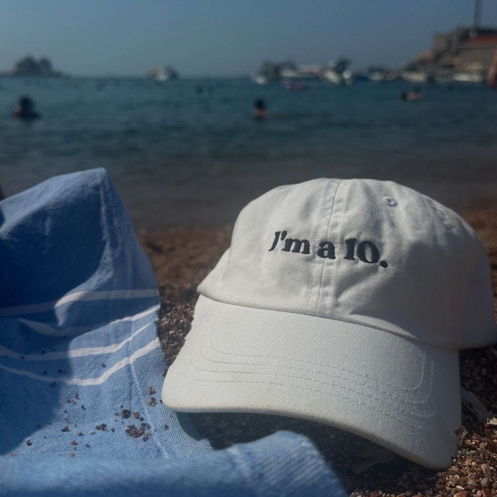 White cap with "I'm a 10." text on a beach with a blue towel.