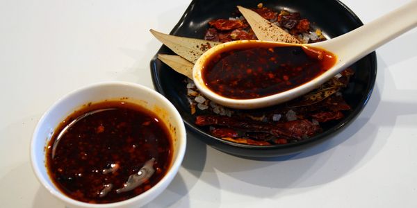 Spicy chili oil in a white bowl and spoon with dried spices on a black plate.