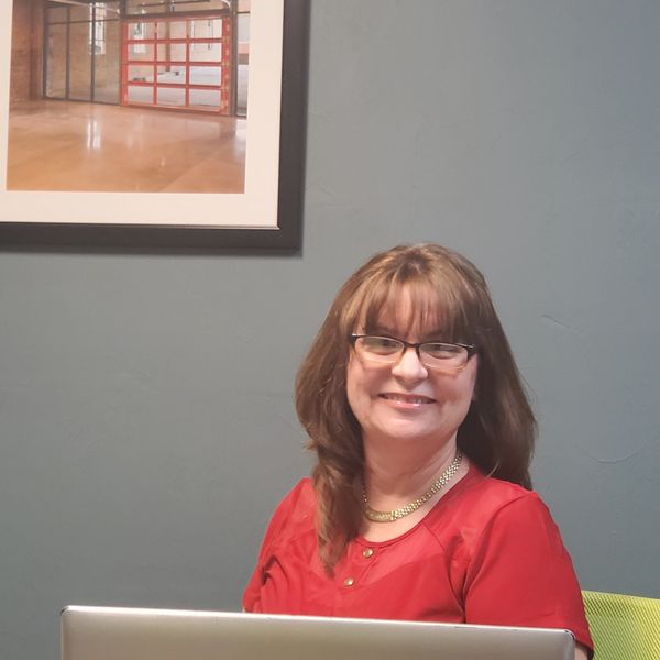 Smiling woman in red blouse sitting at a laptop in an office.