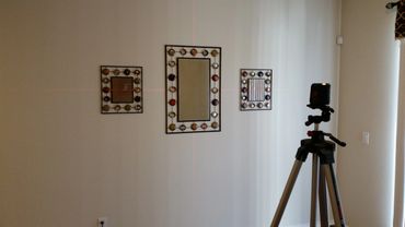Three decorative mirrors arranged on a wall with a tripod and laser level in the foreground.