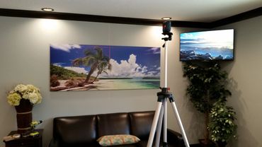 Living room with tropical beach art, TV, and tripod laser level.