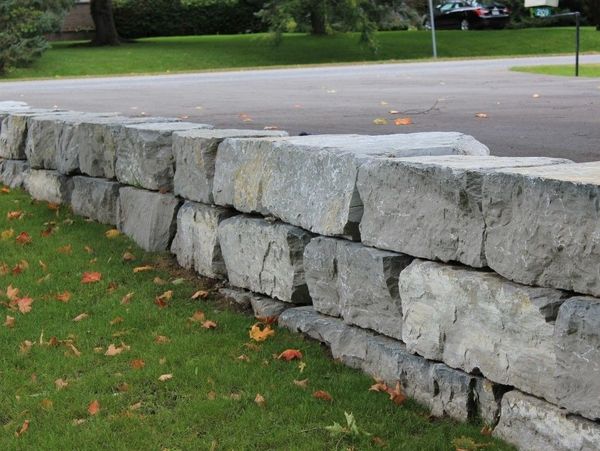A sturdy stone wall separates grassy lawn from a paved area.