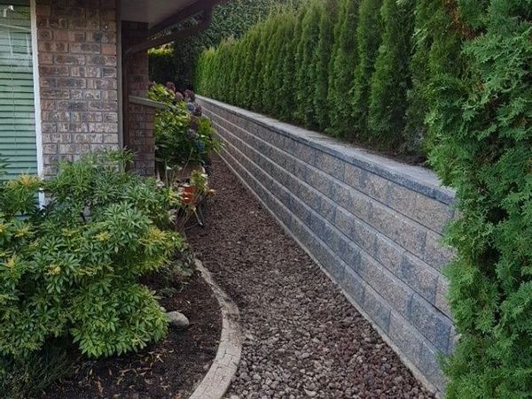 Neatly landscaped backyard with stone retaining wall and lush greenery.