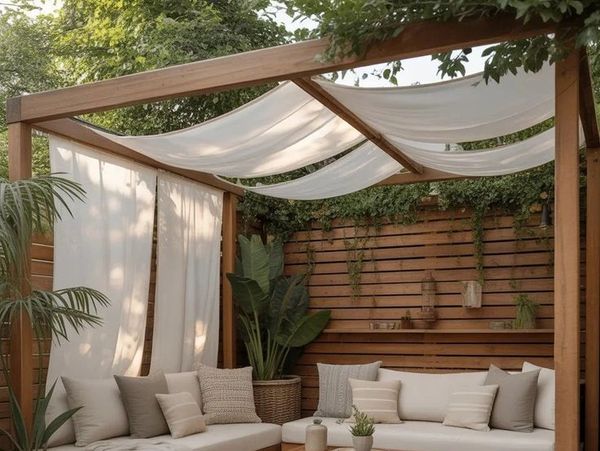Cozy outdoor seating area with wooden pergola and white drapes.
