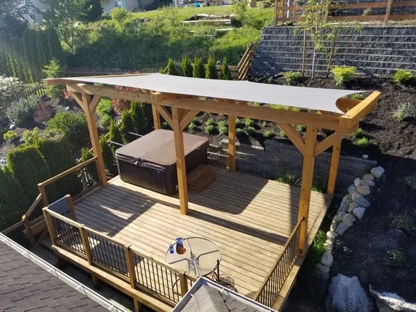 Wooden deck with pergola and hot tub in a landscaped backyard.