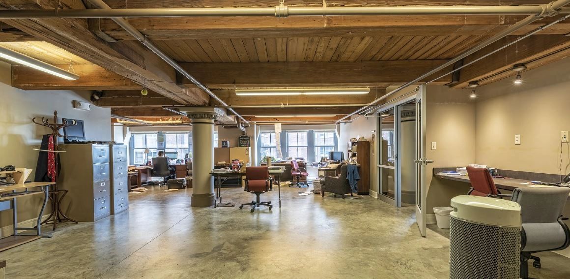 Spacious industrial-style office with wooden beams and large windows.