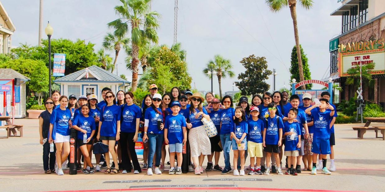 Large group wearing matching blue shirts posing outdoors on a sunny day.