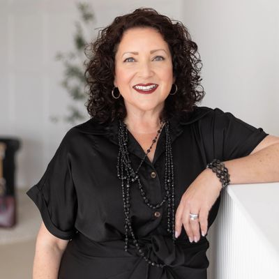 HR Consultant, Maura Richardson, leaning against a mantle, in black dress.