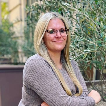 Smiling woman with glasses and long blonde hair outdoors.