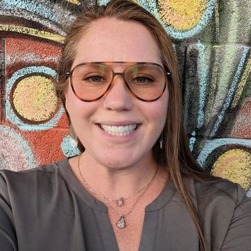 Smiling woman wearing large sunglasses in front of a colorful graffiti wall.