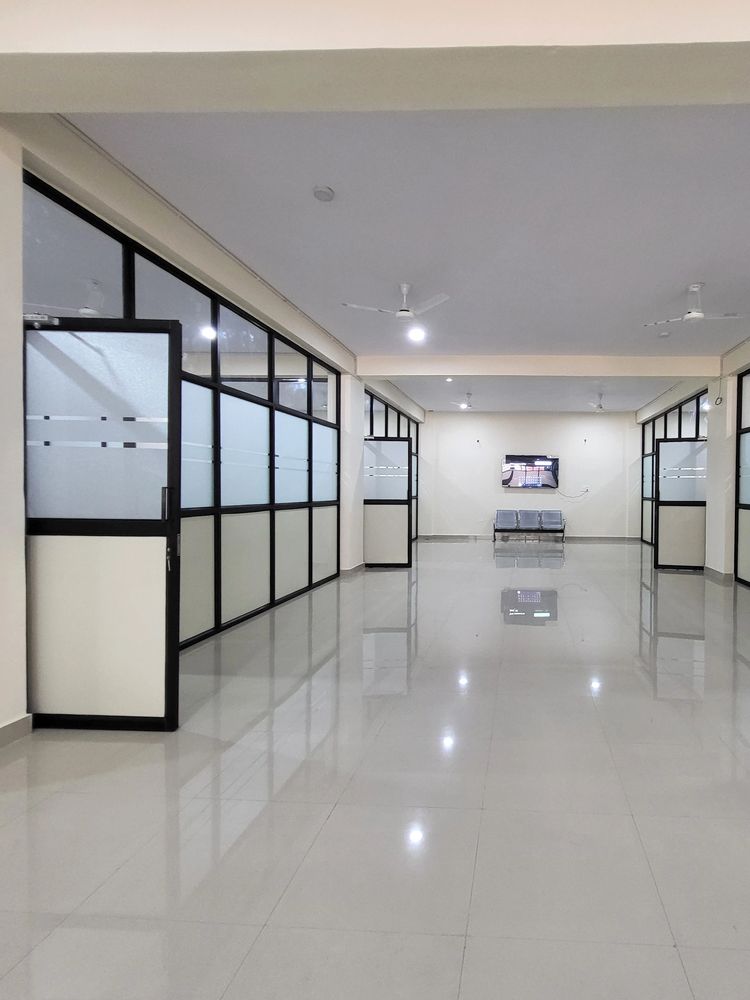 Empty modern office corridor with glass partitions and ceiling fans.